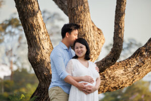 Expectant mother in a flowing dress posing beside jacaranda trees on the UQ St. Lucia campus.